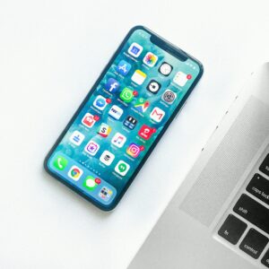 Smartphone met kleurrijke app-iconen naast zilveren laptop op witte ondergrond